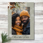 Rustic Snowfall Pine Floral Sage Photo Wedding Save The Date<br><div class="desc">Envelop your guests in the serene beauty of winter with our exquisite photo wedding save the date card. A calming dusty sage backdrop creates a peaceful canvas for a stunning arrangement of fresh green pine sprigs, soft cream-coloured blooms, and rustic brown pinecones. This natural masterpiece is adorned with a delicate...</div>