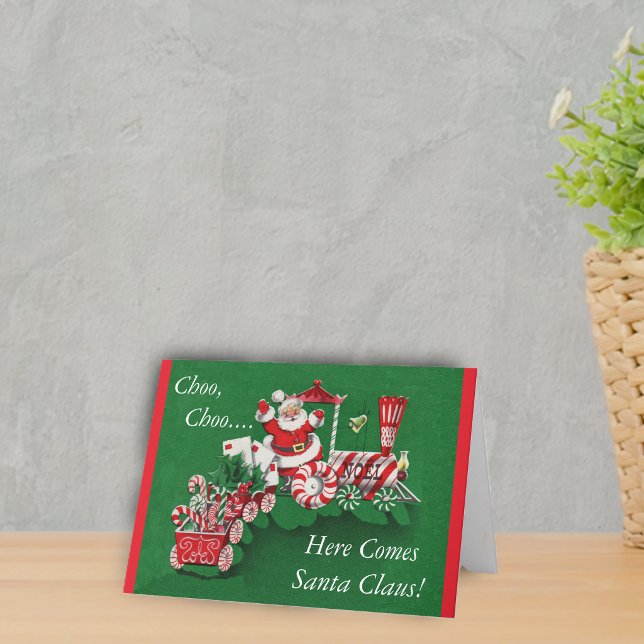 Santa Christmas Train Holiday Card (Santa riding peppermint candy train with letters on a greem Merry Christmas Here comes Santa Card.)
