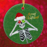 Silly Christmas Skeleton Hat Ornaments Green<br><div class="desc">This hanging ceramic ornament has a silly skeleton holding red and green ornaments up to his eyes while smiling and wearing a fur trimmed red Santa Claus hat on a green background with faux gold glittery specks. Merry Christmas text in gold on the front. Customise your text on the back...</div>