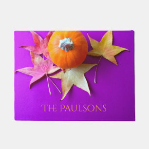 Small pumpkin with fall leaves on purple doormat