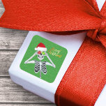 Smiling Christmas Skeleton Ornament Eyes on Green Square Sticker<br><div class="desc">This square sticker has a smiling skeleton wearing a red Santa hat holding up shiny ornaments to his eyes on a green background with tiny gold flecks and the text Merry Christmas in bright gold.</div>