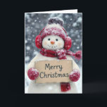 Snowman With a Merry Christmas Sign Card<br><div class="desc">A cheerful snowman,  wearing red earmuffs,  cap,  and a matching scarf,  holds a sign that reads "Merry Christmas" amid a snowy background.
The inside text can be changed.</div>