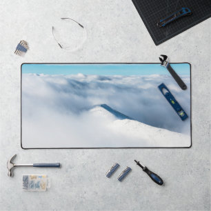 Snowy winter mountain wrapped in clouds desk mat