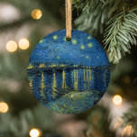 Starry Night Over the Rhône | Vincent van Gogh Ceramic Tree Decoration<br><div class="desc">Starry Night Over the Rhône (1888) by Vincent van Gogh is a mesmerising Post-Impressionist painting that captures a serene nighttime view of the Rhône River in Arles, France. The artwork features a deep blue sky adorned with shimmering golden stars and their reflections on the water. In the foreground, two figures...</div>