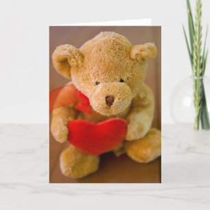 Stuffed teddy bear holding a heart greeting card