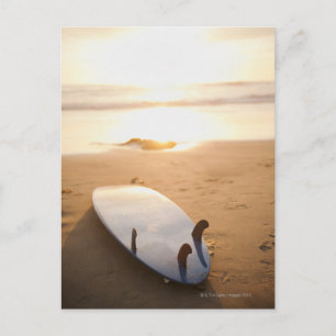 Surfboard laying on beach at sunset postcard