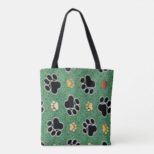 Tan and black paw print on green grass tote bag
