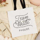 Team Bride Modern Script Gold Wedding Name Tote Bag<br><div class="desc">This modern tote bag with a minimalist casual chic script calligraphy design reading TEAM BRIDE as well as the custom name of your maid of honour or bridesmaid features clean lines to create a sleek and sophisticated appearance. The understated style with the little printed gold heart detail adds a touch...</div>