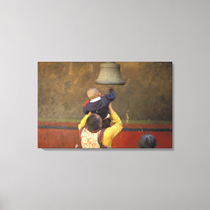 Tibetan Buddhist monk lifting a boy to ring a Canvas Print