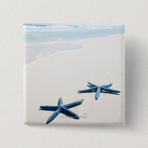 Two blue starfish at water's edge on tropical 15 cm square badge