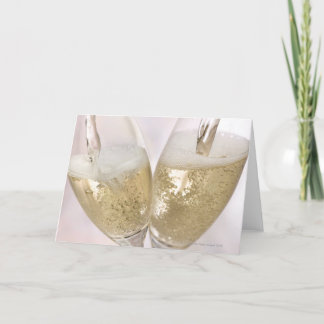 Two champagne flutes being filled with sparkling card