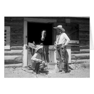 Two cowboys standing next to a barn with a horse