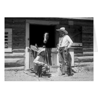 Two cowboys standing next to a barn with a horse