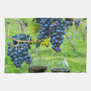 Two hands toasting with red wine near blue grapes tea towel