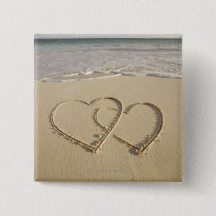 Two overlying hearts drawn on the beach with 15 cm square badge