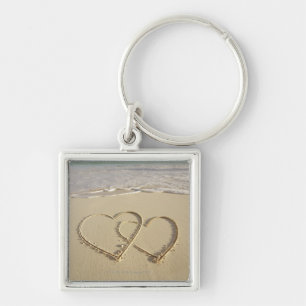Two overlying hearts drawn on the beach with key ring
