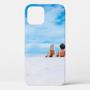 Two women lying on white sand facing beach under b iPhone 12 case