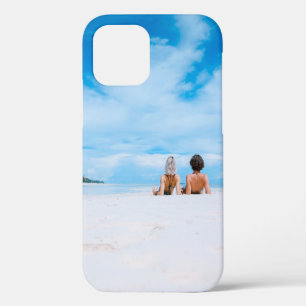 Two women lying on white sand facing beach under b iPhone 12 case