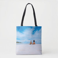 Two women lying on white sand facing beach under b