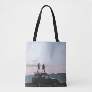 Two women standing on car's roof tote bag