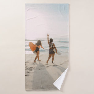 Two women walking towards the ocean carrying surfb bath towel