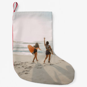 Two women walking towards the ocean carrying surfb small christmas stocking