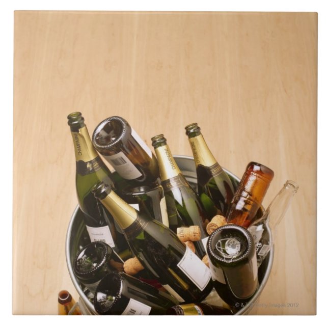 Waste bin full of empty champagne bottles on tile (Front)