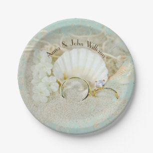 wedding rings and seashells in sand with net paper plate