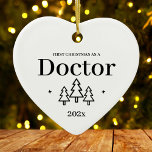 White Heart Doctor First Christmas Ornament<br><div class="desc">First Christmas as a doctor heart ornament for a new job and graduation from medical school. Elegant porcelain ceramic holiday ornaments in white with black lettering. Featuring Christmas trees and stars.</div>