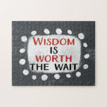 Wisdom Is Worth The Wait Jigsaw Puzzle<br><div class="desc">Bold text reading "Wisdom Is Worth The Wait" is centred against a grey background. The black and red text sits on a white rectangle with large textured white dots around it,  providing a playful contrast against the solid colour backdrop.</div>