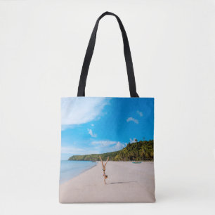 Woman doing acrobatic on seashore near mountain ra tote bag