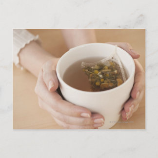 Woman holding cup with chamomile tea postcard