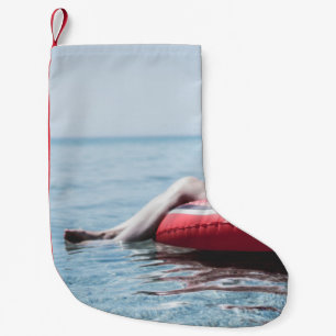 Woman on an inflatable float in the ocean pointing small christmas stocking