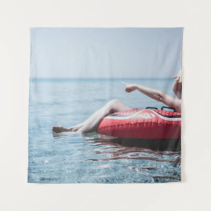Woman on an inflatable float in the ocean pointing tapestry