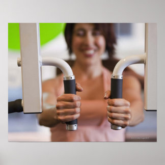 Woman using exercise machine in gym poster