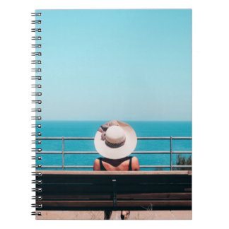 Woman wearing white straw hat sitting on bench loo notebook