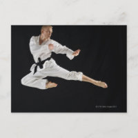 Young man performing karate kick on black