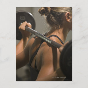 Young woman exercising with barbell, rear view postcard