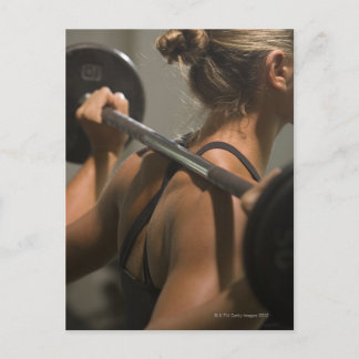 Young woman exercising with barbell, rear view postcard