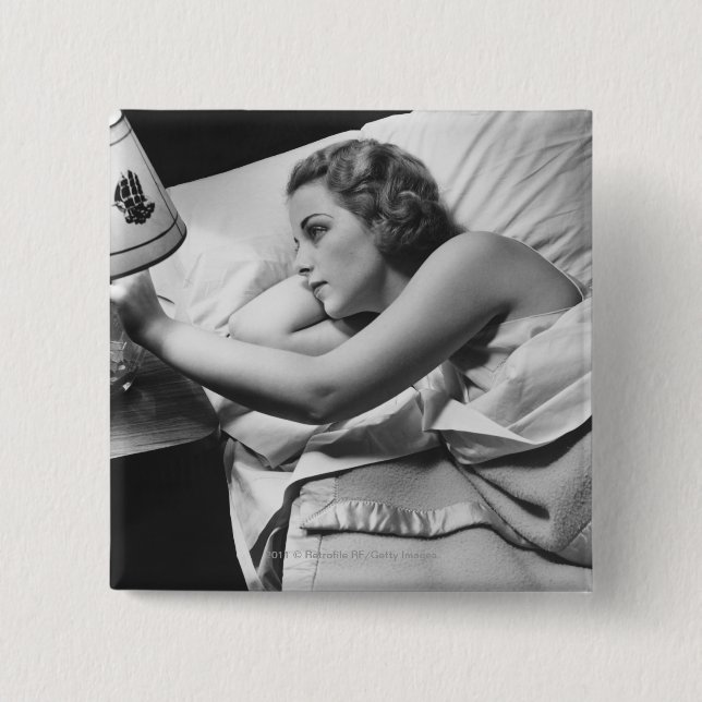 Young woman lying on bed turning off lamp on 15 cm square badge (Front)