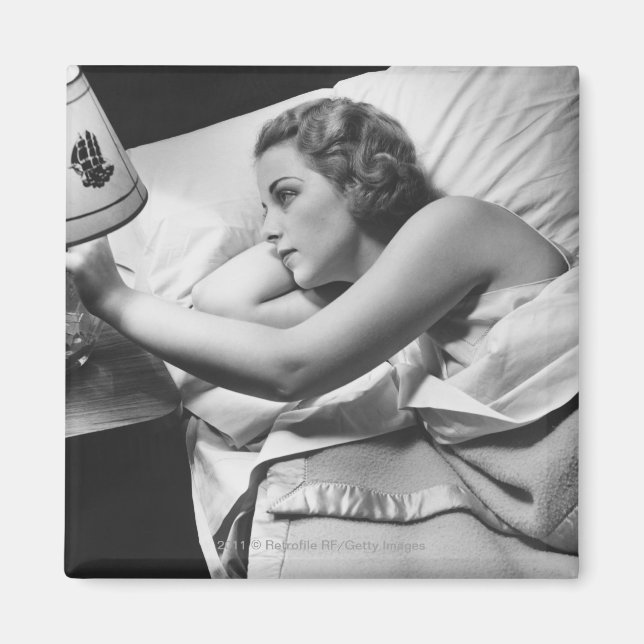 Young woman lying on bed turning off lamp on magnet (Front)