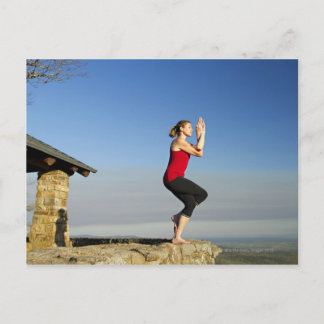 young woman practices yoga on a bluff in the postcard